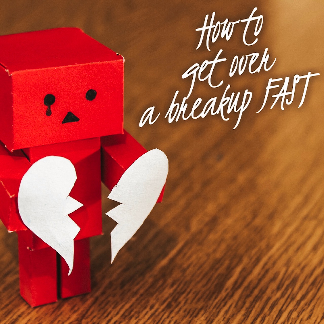 A robot made of paper holding a broken heart with a tear coming from its eye. It says "How to get over a breakup FAST."