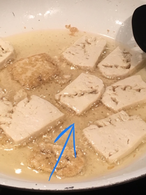 How to cook perfect tofu every time - Tofu slices cooking in a pot where the softer top side is slightly bending out because the bottom is shrinking from being cooked.