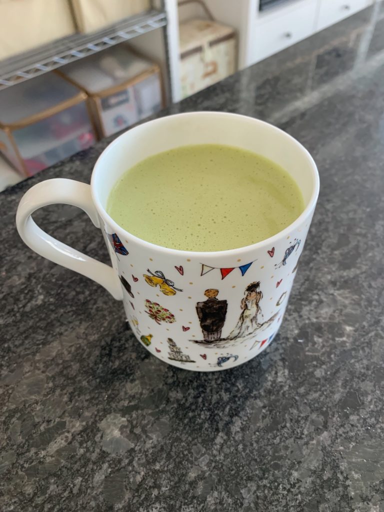 A picture of a matcha latte in a china mug with an illustration of a bride and groom from behind with doodles of wedding-related items around them. 
